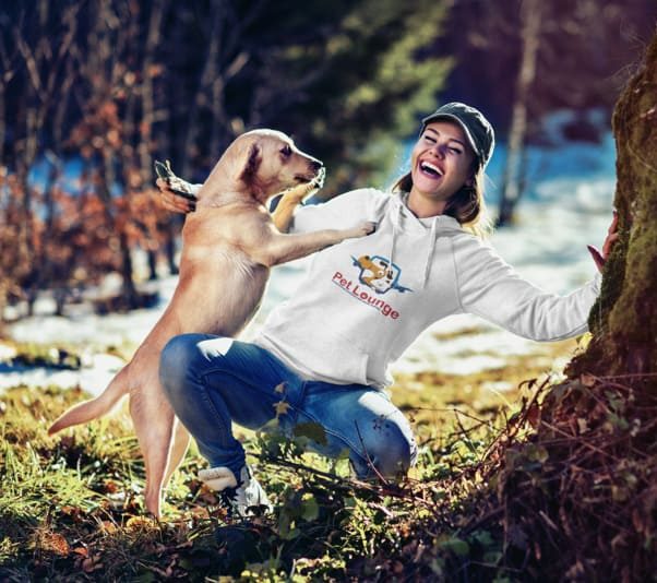 A woman in a "Pet Lounge" hoodie playing outdoors with a jumping golden retriever.